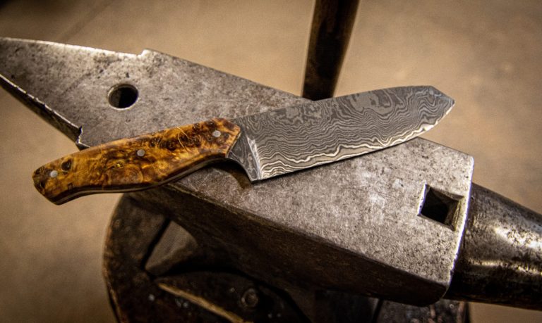 Ein Messer mit Holzgriff liegt auf einem Amboss.