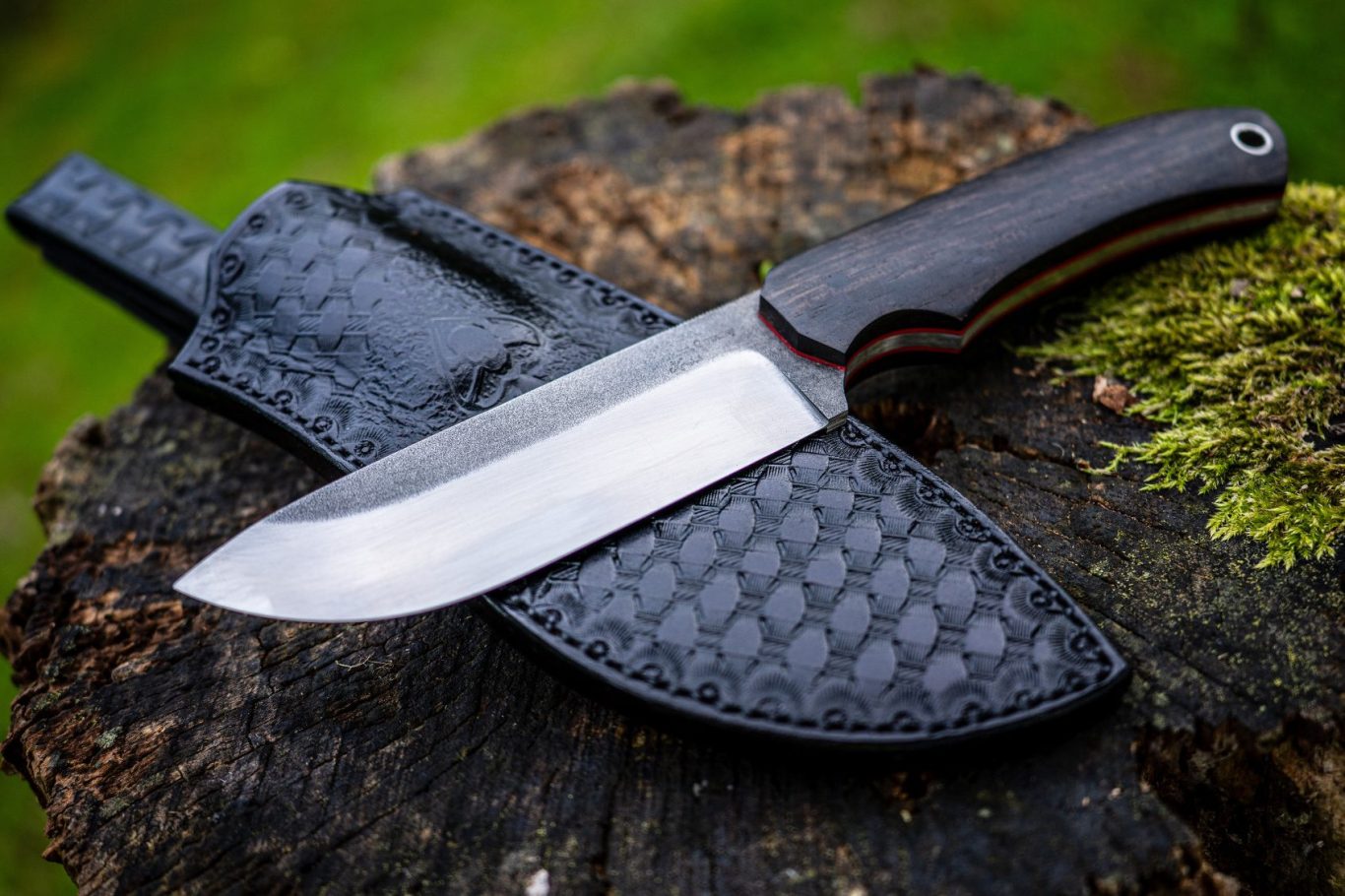 Ein großes Bushcraftmesser mit dunkler Klinge und schwarzer Lederscheide auf einem Baumstumpf.