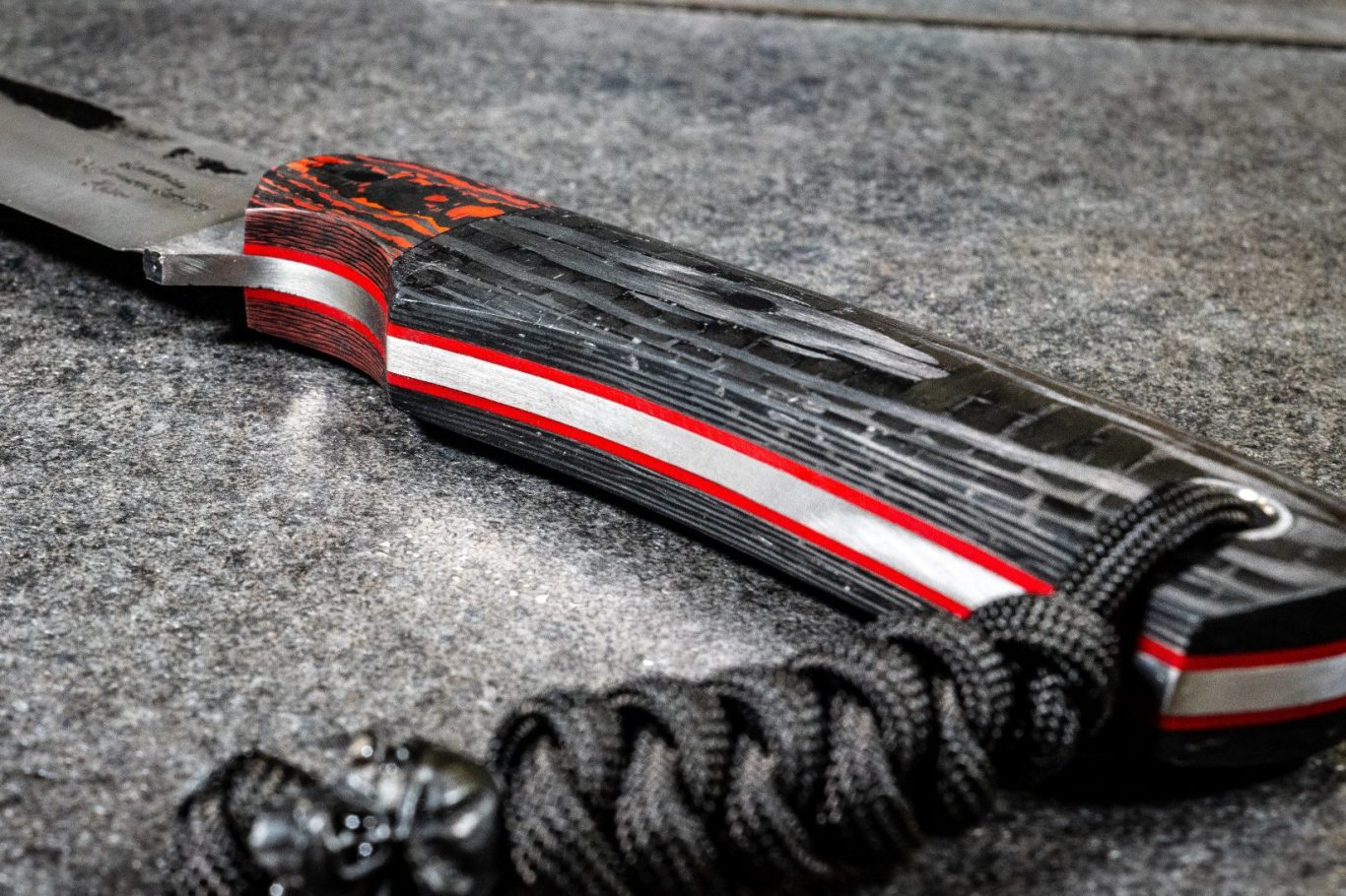 Schwarzer Messergriff mit rot-weißen Akzenten und paracord-artigem Griffband.